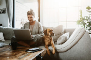 a lady sitting on the couch and working with her dog sitting next to her